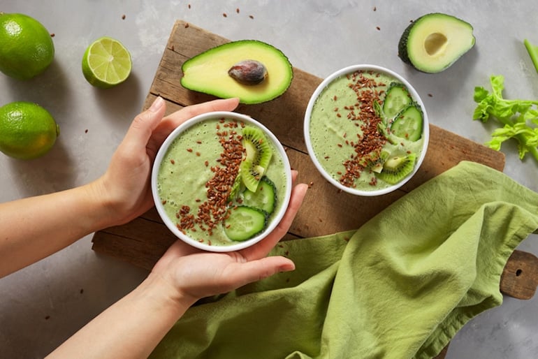 Woman holding a smoothie bowl made with avocado and flaxseed, two of the best foods for hormone balance