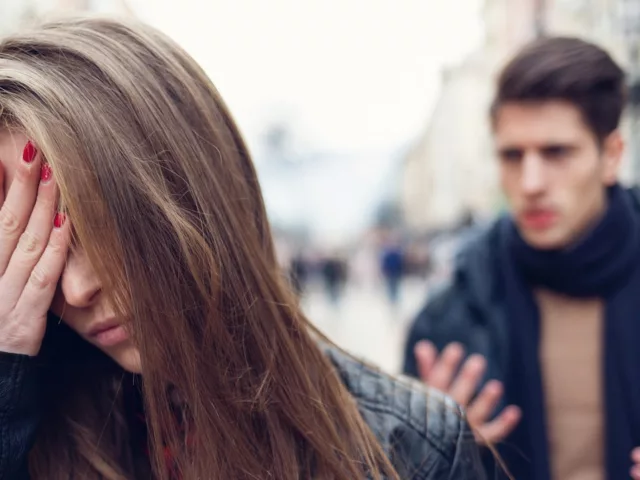 Woman wincing in pain on the street because her narcissist boyfriend is yelling