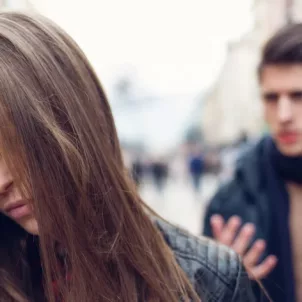 Woman wincing in pain on the street because her narcissist boyfriend is yelling