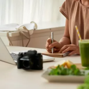 Woman writing a food diary at her kitchen table, planning to start an elimination diet