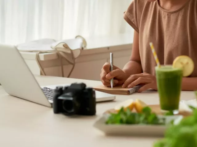 Woman writing a food diary at her kitchen table, planning to start an elimination diet