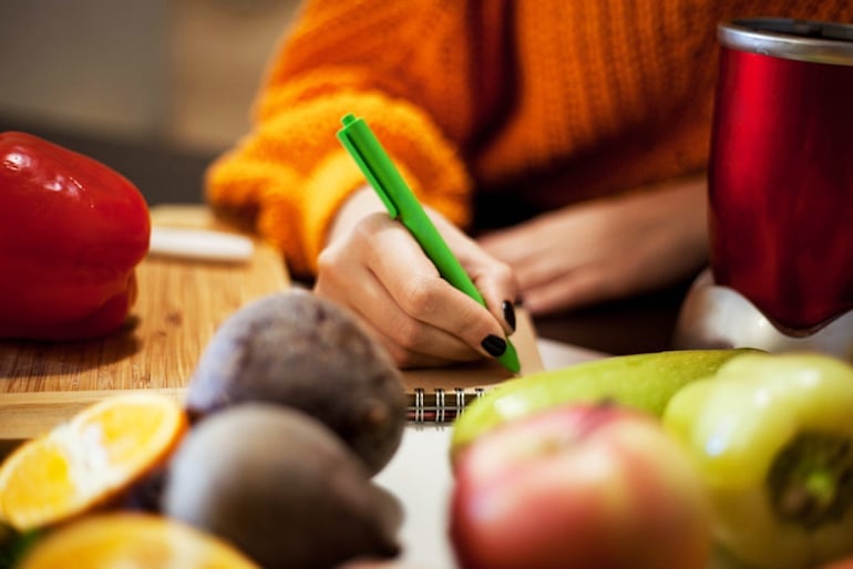 Woman in kitchen writing a food diary, planning to start her elimination diet