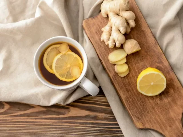 Lemon ginger tea in a white mug next to a wooden board with fresh ginger and lemon