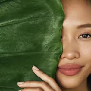 beautiful woman who made plant-based skincare swaps half hidden behind a big leaf