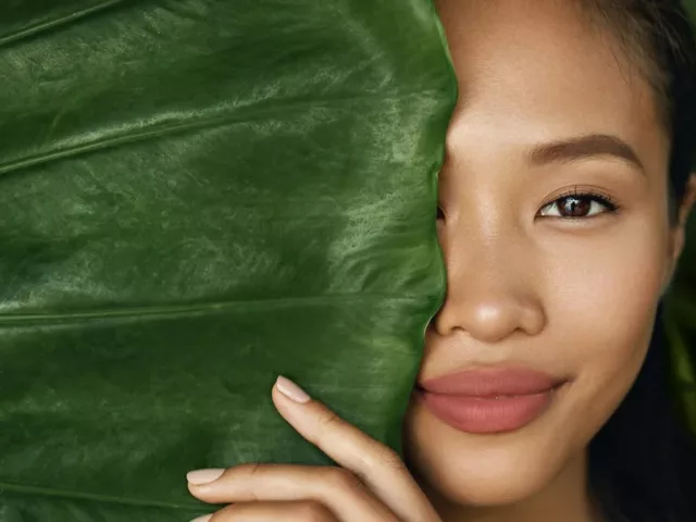 beautiful woman who made plant-based skincare swaps half hidden behind a big leaf