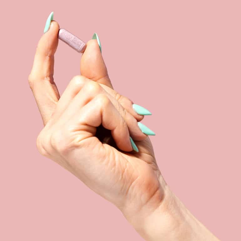 Woman's hand holding HUM Nutrition Private Party vaginal probiotic in front of pink background