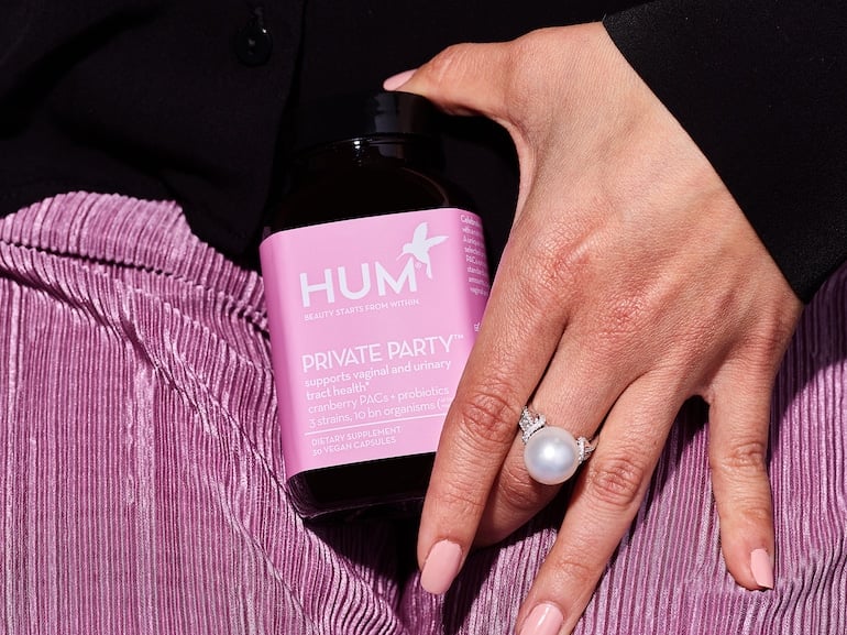 Woman's hand holding HUM Private Party vaginal probiotic supplement in front of her purple skirt