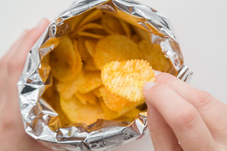 Woman's hand reaching into a bag of potato chips to satisfy her salty food craving