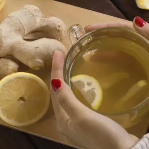 Woman with red nail polish holding mug of fresh lemon ginger tea