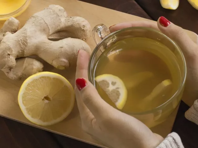 Woman with red nail polish holding mug of fresh lemon ginger tea