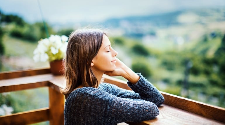 Woman on balcony with eyes closed, recognizing the importance of alone time and pleasant solitude