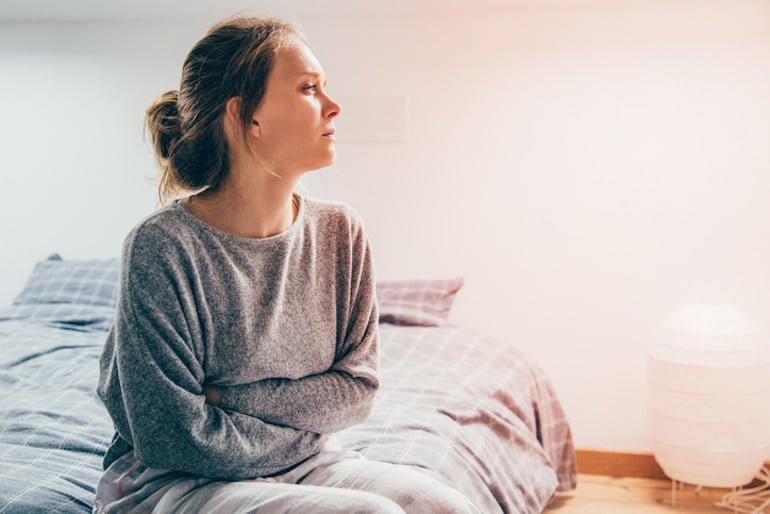 Woman clutching her stomach sitting in bed, suffering from candida overgrowth symptoms