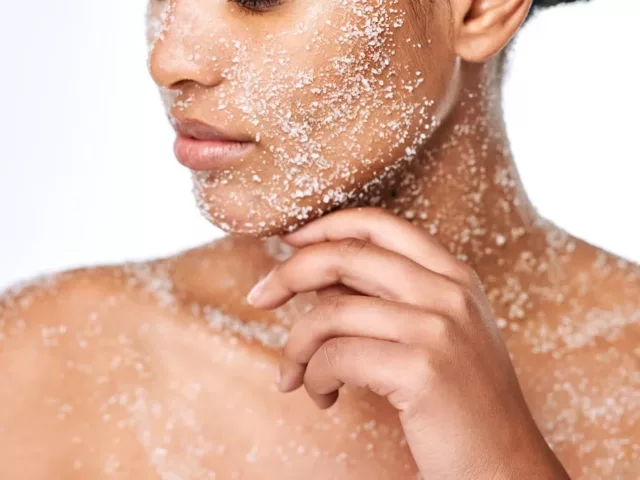 Woman using physical exfoliants on her face, neck, and decolletage