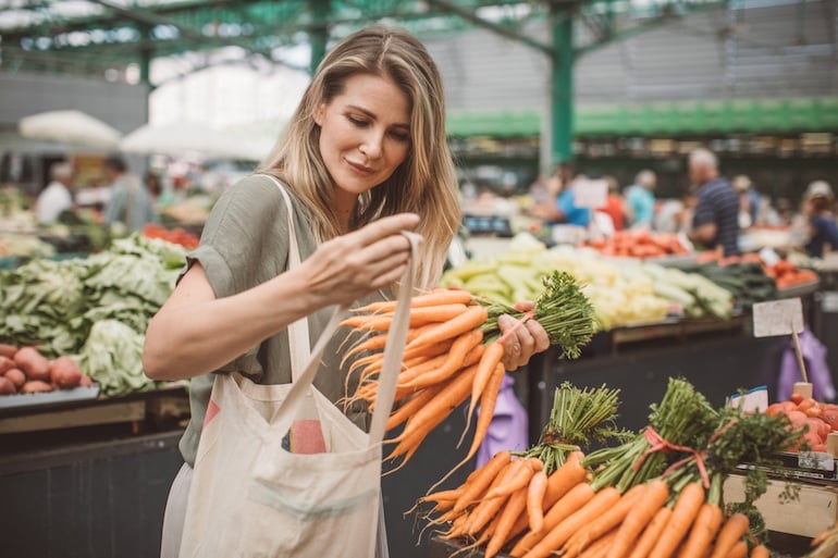 Woman putting carrots, one of the longest-lasting produce items, in cloth bag at farmers market