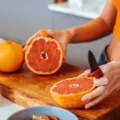 Woman in orange top slicing citrus fruit to reap benefits of vitamin C on her immune system