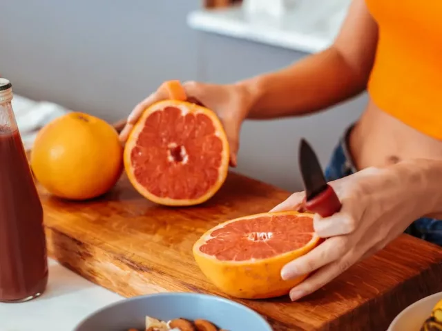 Woman in orange top slicing citrus fruit to reap benefits of vitamin C on her immune system