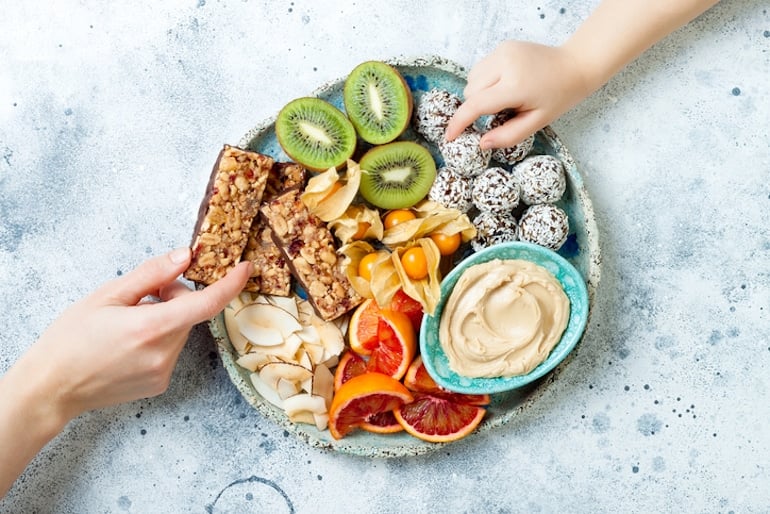 Two people reaching for healthy snacks, like kiwi and energy balls, to beat sugar cravings