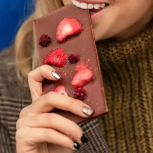 Woman giving into her sugar craving by biting into chocolate bar covered in berries