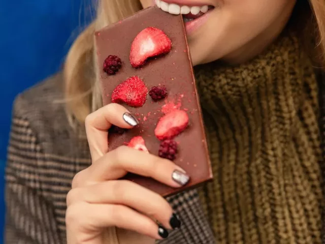 Woman giving into her sugar craving by biting into chocolate bar covered in berries