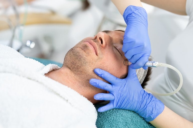 Facialist performing exfoliating microdermabrasion treatment on a young man