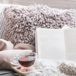 Cozy social distancing sanctuary on couch with pillows, blankets, book, and tea