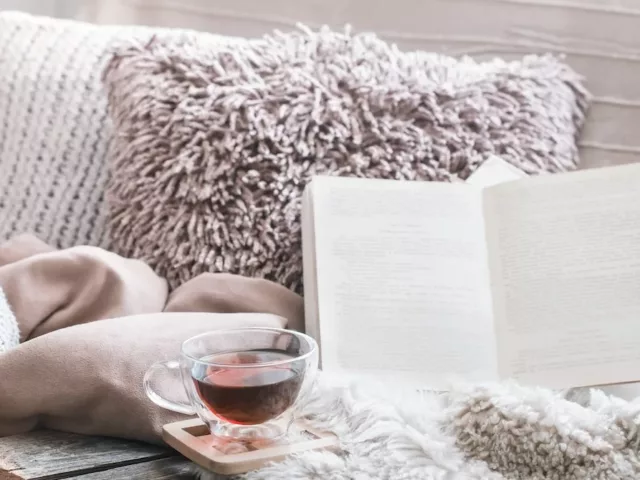 Cozy social distancing sanctuary on couch with pillows, blankets, book, and tea