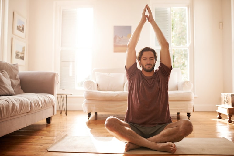 Man meditating on yoga mat in his home, which he turned into a calming social distancing sanctuary