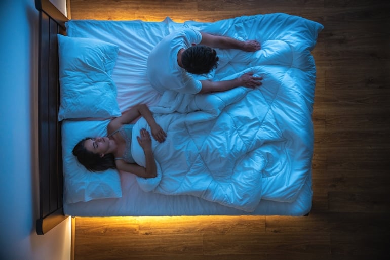 Couple in bed with the man sitting upright due to insomnia