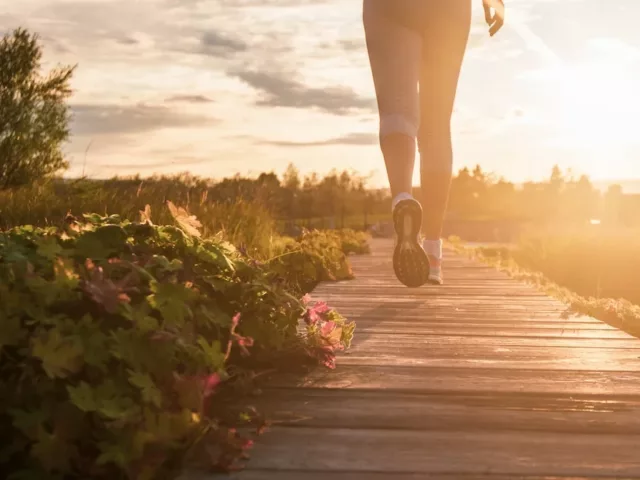 Woman walking on a wooden path in nature before dusk to reap the surprising benefits of walking daily