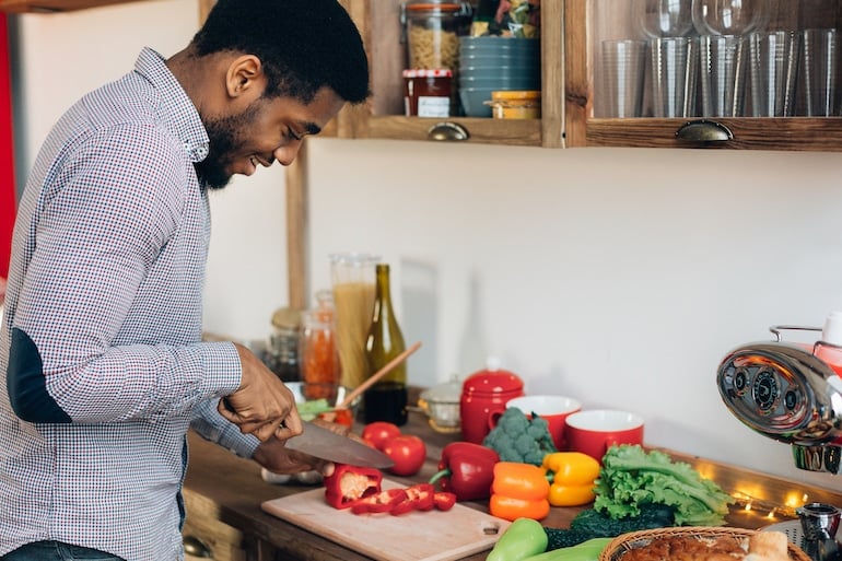 Man cutting bell peppers and other produce in kitchen to prepare to freeze