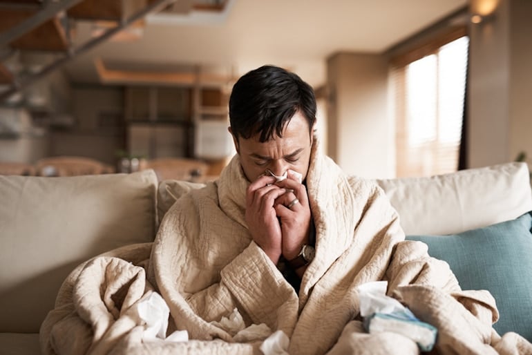 Man blowing nose under covers on couch, who needs vitamin D for immune support