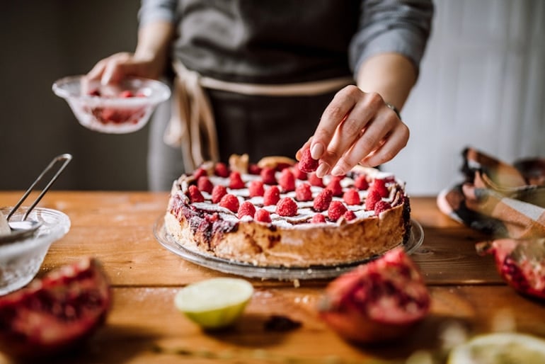 Woman adding raspberries to a sugar filled cake