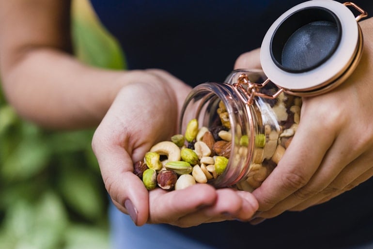 Woman pouring assorted nuts from glass container, which are rich in magnesium to help relieve constipation