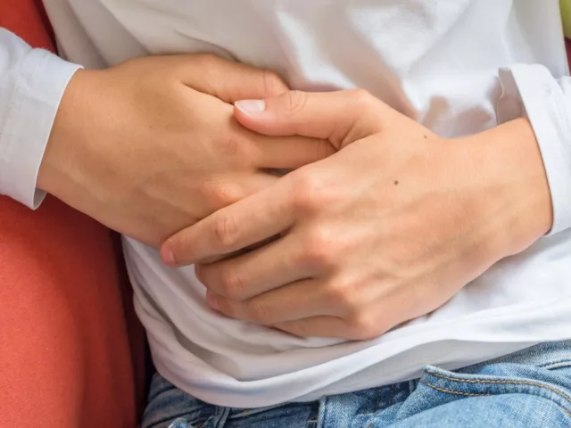 Man feeling unwell on couch touching his stomach to emphasize connection between gut health and immune system