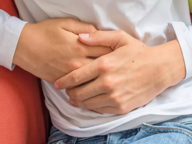 Man feeling unwell on couch touching his stomach to emphasize connection between gut health and immune system