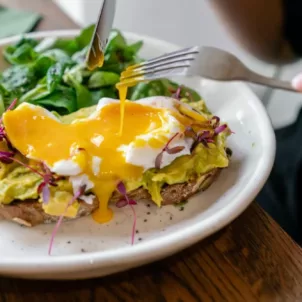 Woman eating a healthy breakfast for weight loss, cutting into an egg sandwich with avocado and leafy greens