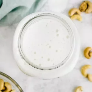 Homemade nut milk in a glass jar next to bowl of cashews and blue kitchen cloth