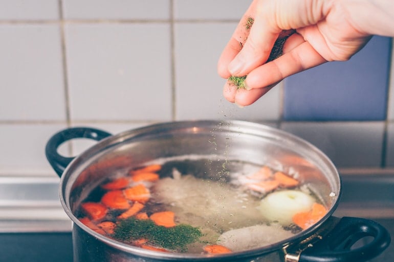 Woman putting spices into soup for her bland diet meal for heartburn prevention