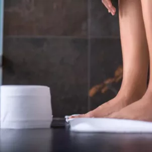 Woman sitting on toilet next to a roll of toilet paper