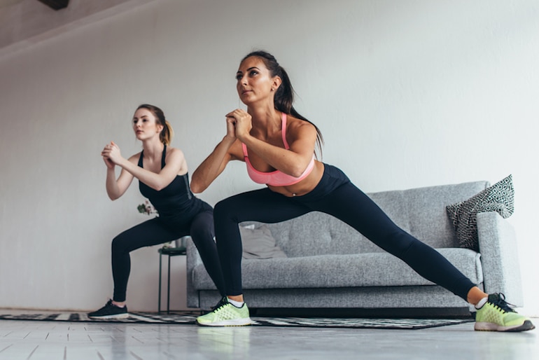 Two women doing side lunges at home before their workout