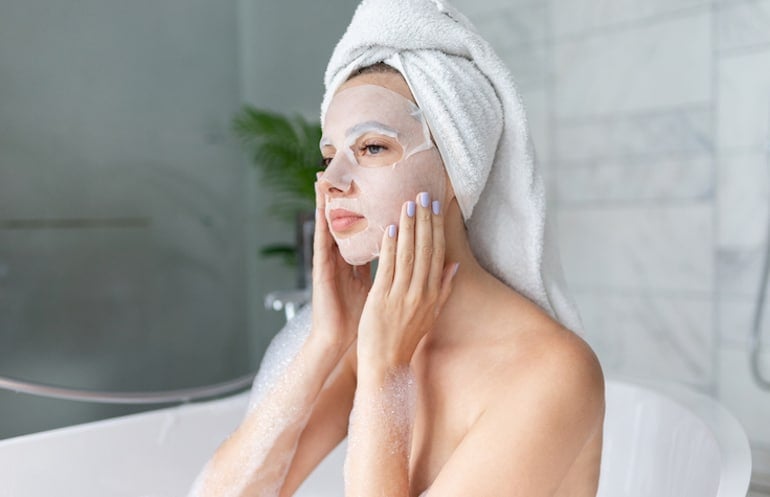 Woman in bath wearing a sheet mask, one of the most popular parts of the best K-beauty routine