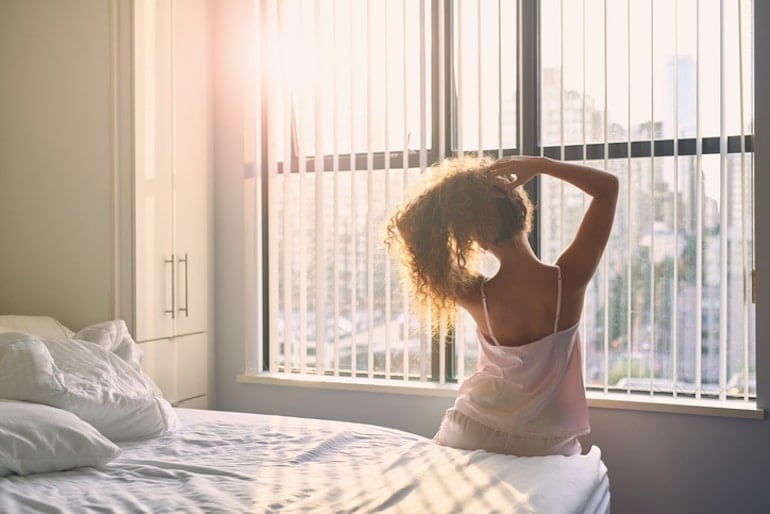 Woman sitting up and stretching in bed in the morning looking out the window