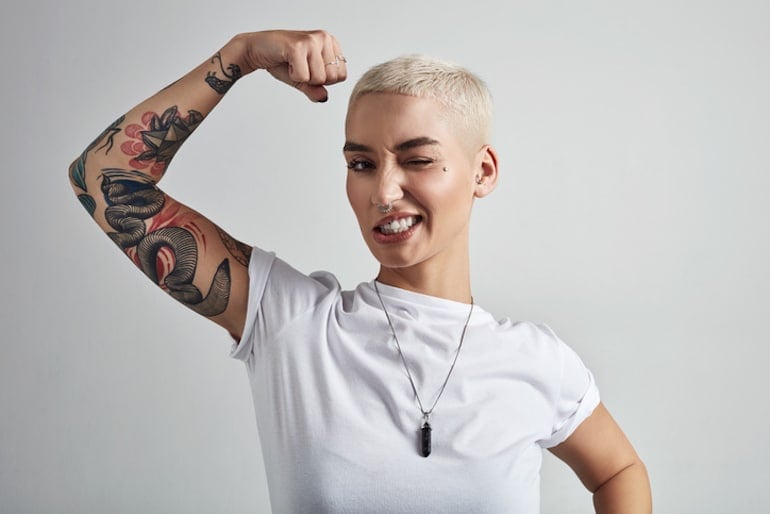 Woman flexing her biceps and winking, showing off her confidence after practicing the best self-love tips guided by Anna Sweeney