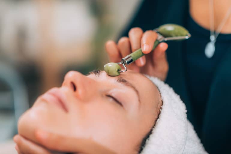 Woman getting a facial with a jade roller cooled from the aesthetician's fridge for skincare