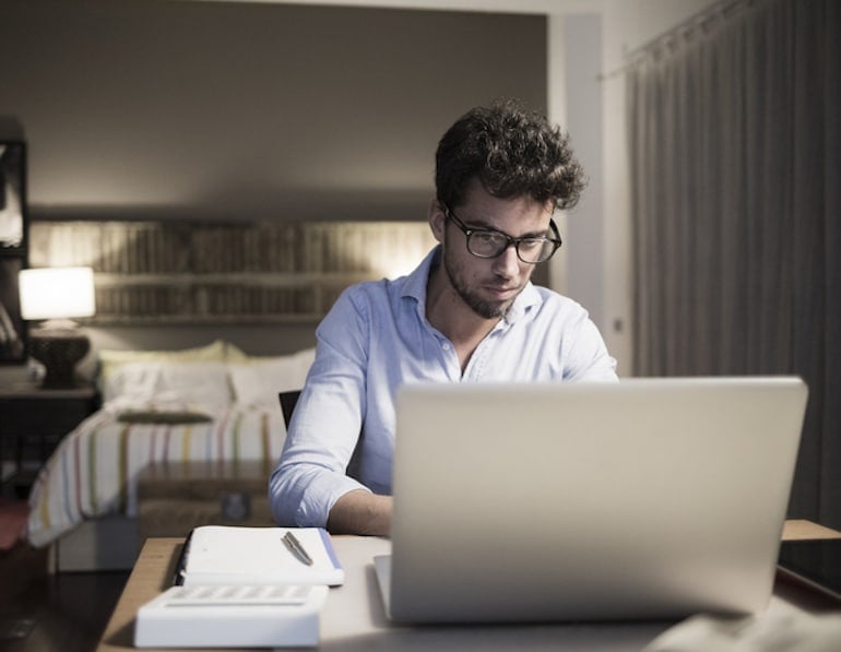 Man working on his laptop in the home office section of his bedroom