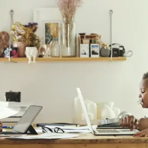 Young parents working from home on laptops in kitchen while the father holds a baby, needing to find work-life balance