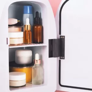 Mini skincare fridge cooling beauty products in front of pink backdrop with palm leaves