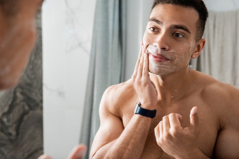 Man moisturizing his skin in the mirror to prevent breakouts and promote clear skin