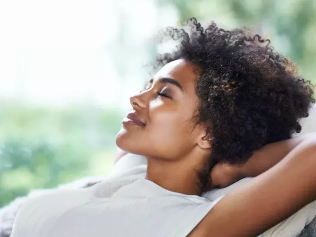 Woman with eyes closed relaxing on couch and practicing self-love