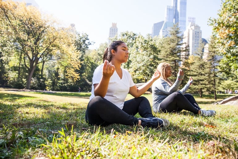 Two women meditating outdoors on the grass, connecting with their breath and each other for self-love and support